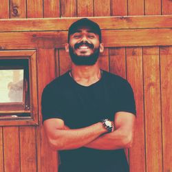 Portrait of smiling young man standing against wooden wall