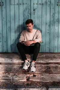 Young man sitting on wood against wall