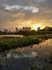 Scenic view of lake by buildings against sky during sunset