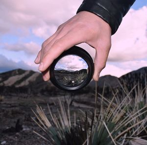 Close-up of man holding lens against sky