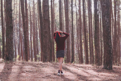 Rear view of woman standing amidst trees in forest