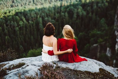 Rear view of women sitting on rock at mountain