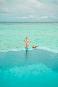 A hand of a woman in swimming pool against sea