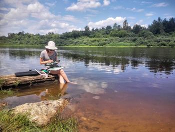 Man sitting in lake against sky