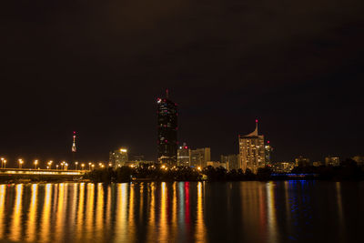 Illuminated buildings by river against sky at night