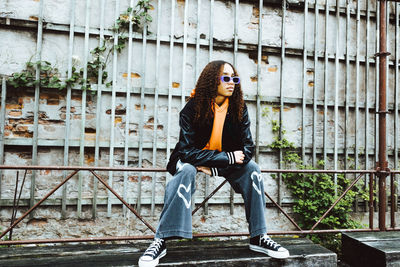 Teenage girl with sunglasses sitting on railing against wall