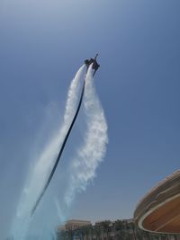 Low angle view of man flyboarding against clear blue sky