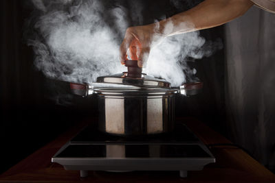 Cropped image of hand opening lid of pressure cooker in kitchen