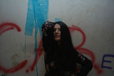 Portrait of woman with hand in hair against graffiti wall