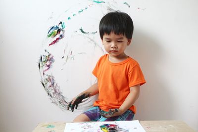 Asian boy select a colour in a paint mixing palette to paint on the concrete wall of the room.