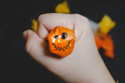 Close-up of hand holding orange leaf against black background