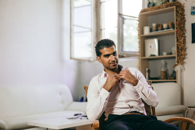 Smiling young man looking away while sitting on chair at home