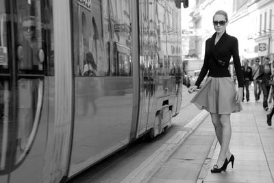 Beautiful woman standing on sidewalk by tram in city