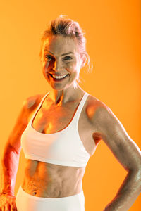 Portrait of young woman standing against yellow background