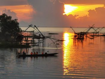 Silhouette people fishing in sea against orange sky