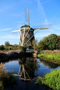 Traditional windmill by lake against sky