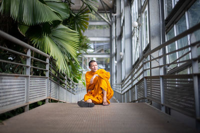 Full length of monk sitting on footpath