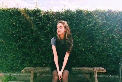 Thoughtful woman sitting on bench against plants