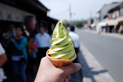 Cropped hand holding ice cream cone on street