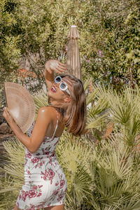 Portrait of smiling young woman wearing sunglasses standing by plants