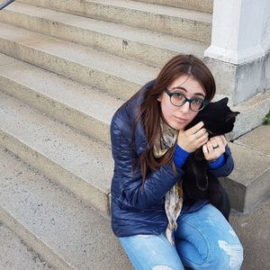 Portrait of young woman sitting with black cat on steps