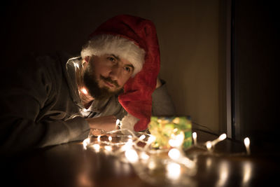 Close-up of young man by illuminated christmas lights on gift in darkroom