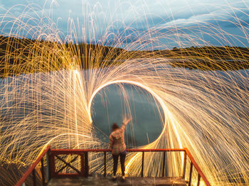 Full length rear view of woman spinning wire wool by lake during dusk