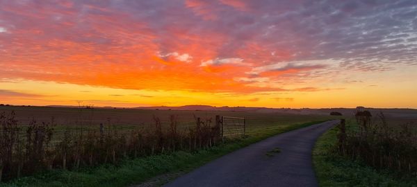 Road amidst field against sky during sunset