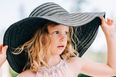 Candid close up portrait of a young girl stood outside with a sun hat