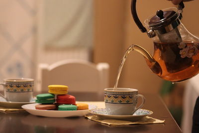 Tea pouring into cup with macaroons on table