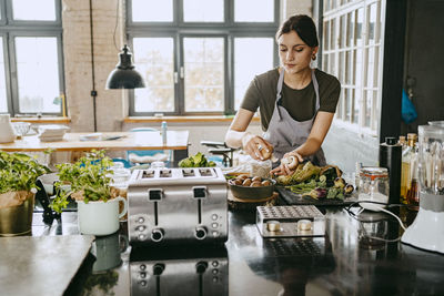 Female chef picking up mushrooms while working in studio kitchen