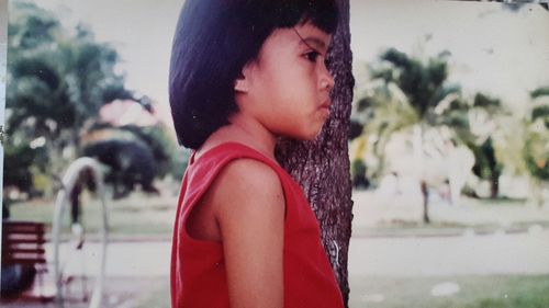 Side view of girl standing against tree