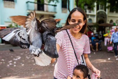 Smiling mother playing with pigeons by son in city