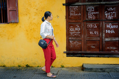 Side view of young woman standing on road against wall