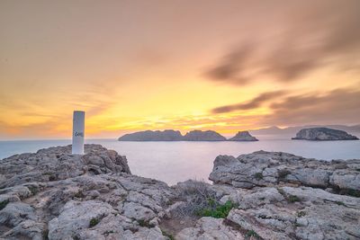 Rocks by sea against sky during sunset