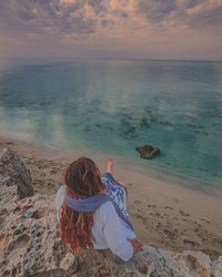 Rear view of woman sitting at beach during sunset