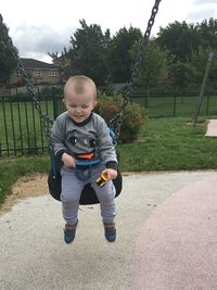 Playful baby boy sitting on swing at park