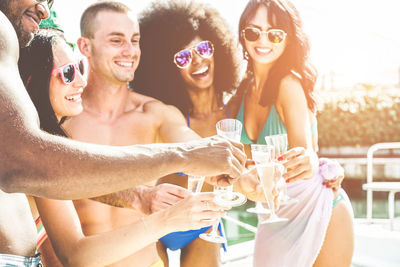 Happy friends toasting drinking glasses in sunny day