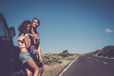 Portrait of young couple standing on road against sky during sunny day
