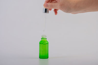 Close-up of hand holding bottle against white background