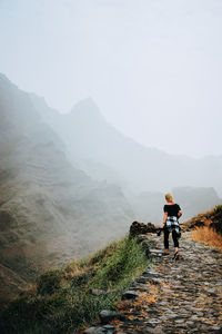 Rear view of man walking on mountain against sky