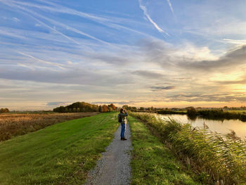 Woman standing on dike and looking over rural land at sunrise