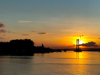 Silhouette bridge over river against sky during sunset