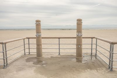 Showers by railing at beach against cloudy sky