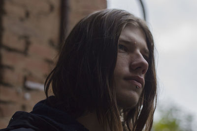 Close-up of thoughtful young man against brick wall