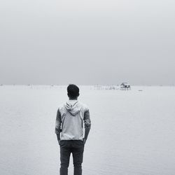 Rear view of mid adult man standing on sand at beach against sky