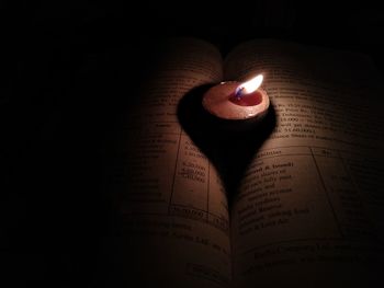 Close-up of lit candles on book in darkroom