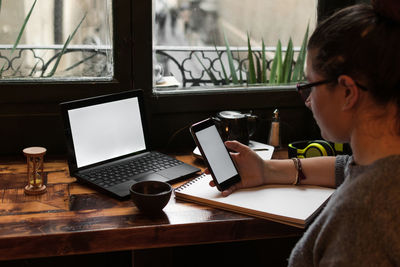 Young woman looks at her phone while studying in a retro pub