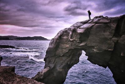 Man on cliff by sea against sky