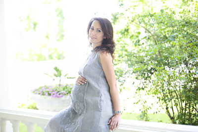 Portrait of pregnant woman woman sitting by railing against plants